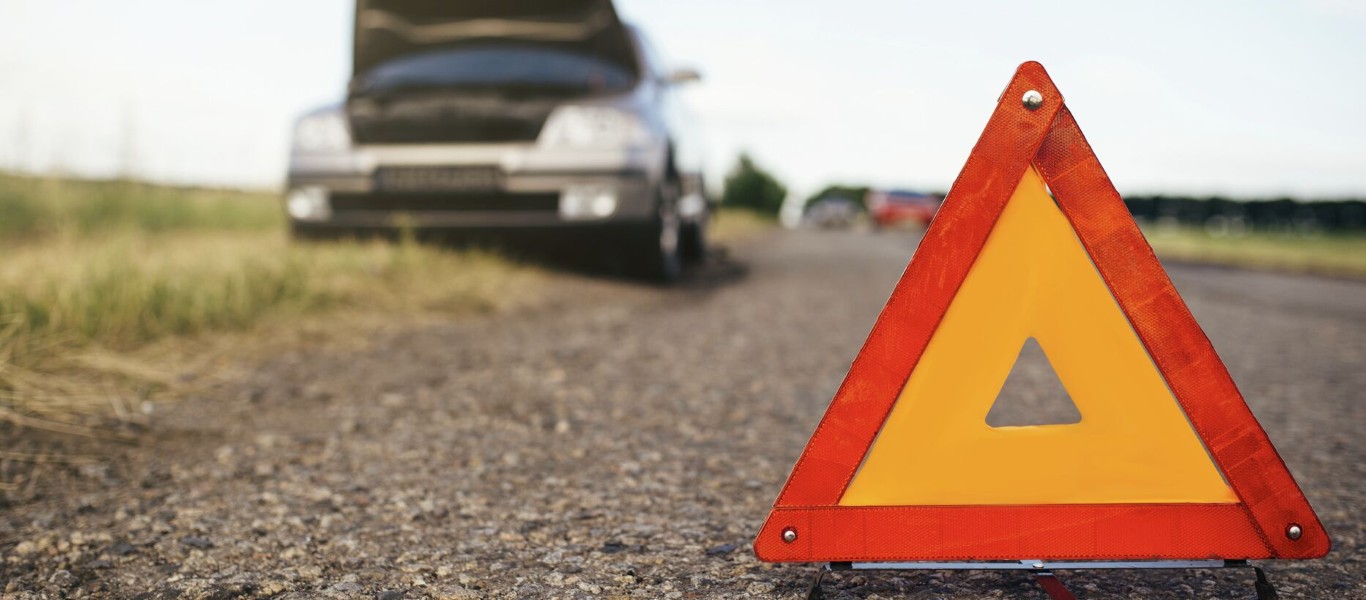Red warning triangle placed on road with a broken-down car in the background