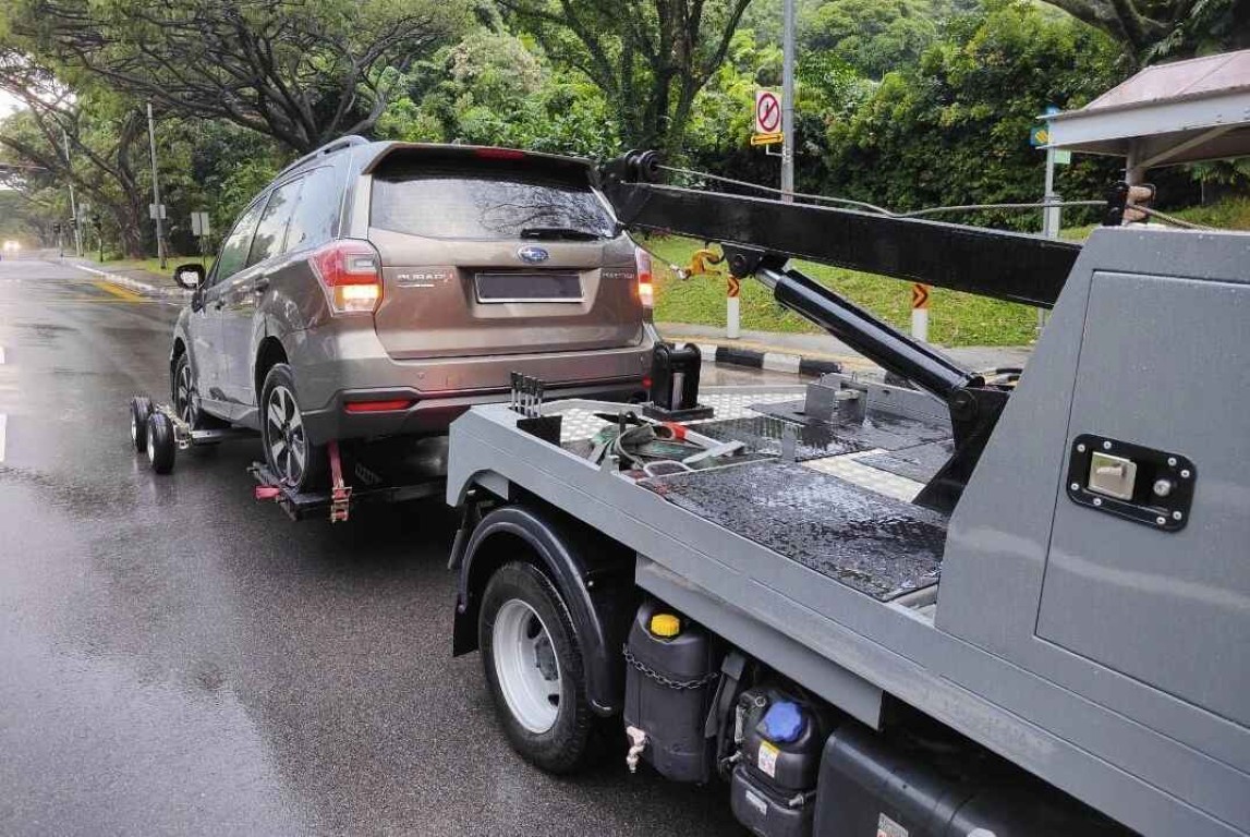 Tow truck assisting a Subaru SUV on a rainy road after a flat tire in Amityville, NY
